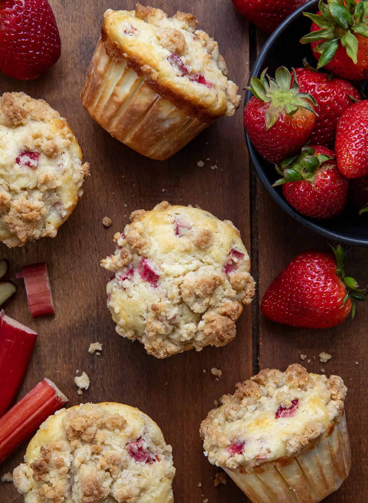 Strawberry Rhubarb Muffins are the perfect sweet-tart treat for spring and summer! Each soft, buttery muffin is packed with fresh strawberries and rhubarb, then topped with a golden crumb! Looking down on Strawberry Rhubarb Muffins on a wooden table with fresh rhubarb and strawberries.