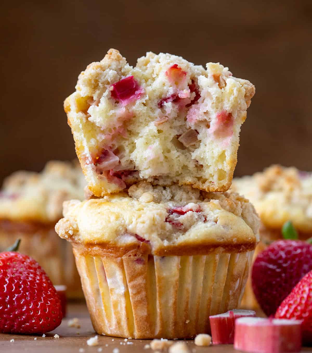 Strawberry Rhubarb Muffins are the perfect sweet-tart treat for spring and summer! Each soft, buttery muffin is packed with fresh strawberries and rhubarb, then topped with a golden crumb! Strawberry Rhubarb Muffins stacked with the top muffin torn in half showing inside texture.