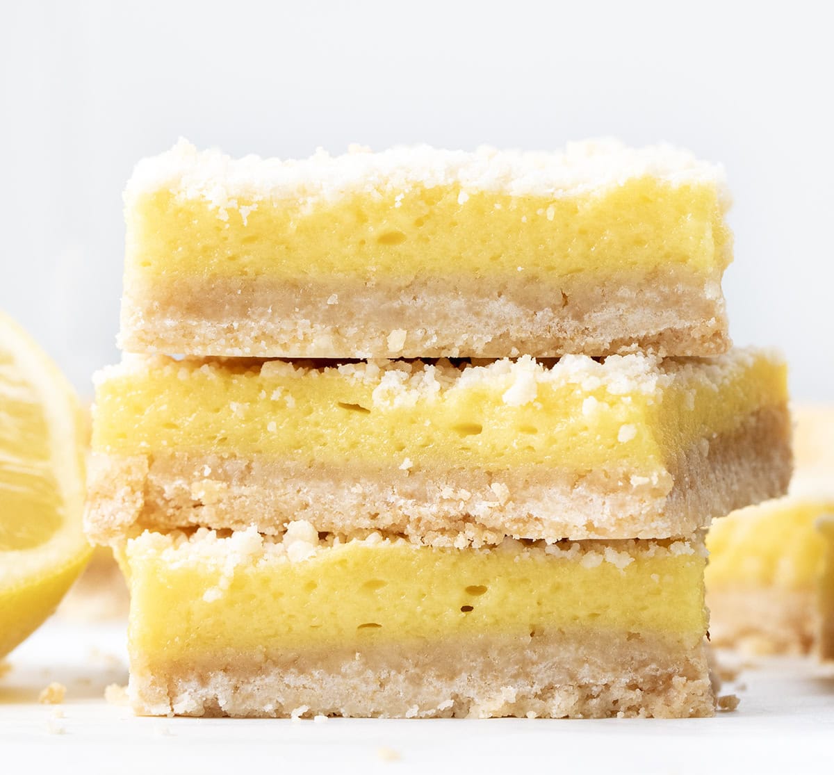 These Sugar Cookie Lemon Bars combine a buttery sugar cookie crust with a creamy, tangy lemonade filling and a golden cookie crumble topping. A refreshing summer dessert thatโs sweet, tart, and irresistibly nostalgic! Stack of Sugar Cookie Lemon Bars on a white table.