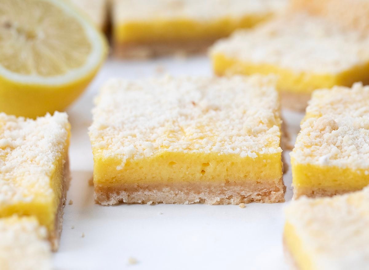These Sugar Cookie Lemon Bars combine a buttery sugar cookie crust with a creamy, tangy lemonade filling and a golden cookie crumble topping. A refreshing summer dessert thatโs sweet, tart, and irresistibly nostalgic! Close up of Sugar Cookie Lemon Bars on a white table.