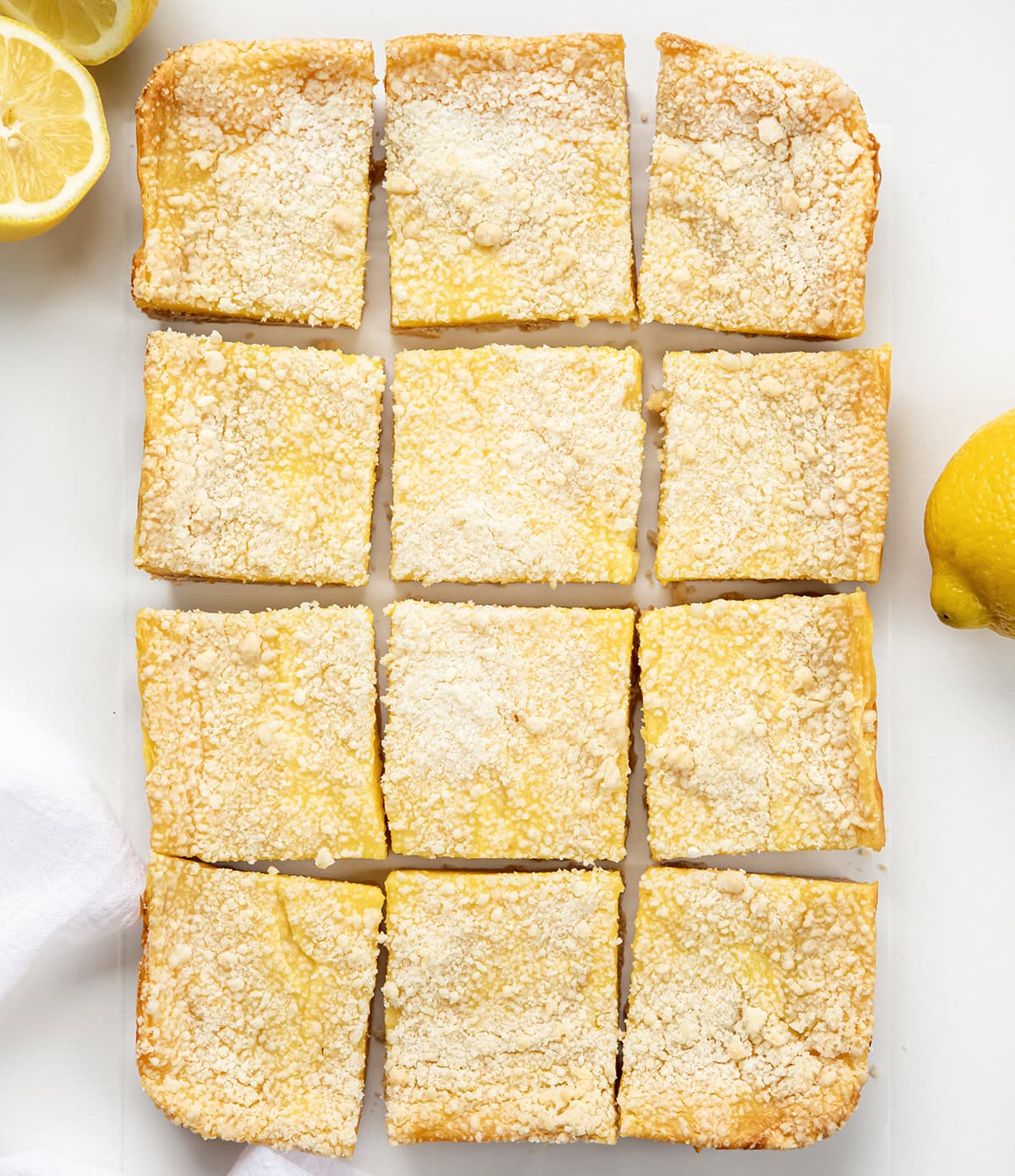 These Sugar Cookie Lemon Bars combine a buttery sugar cookie crust with a creamy, tangy lemonade filling and a golden cookie crumble topping. A refreshing summer dessert thatโs sweet, tart, and irresistibly nostalgic! Looking down on Sugar Cookie Lemon Bars cut into squares on a white table.