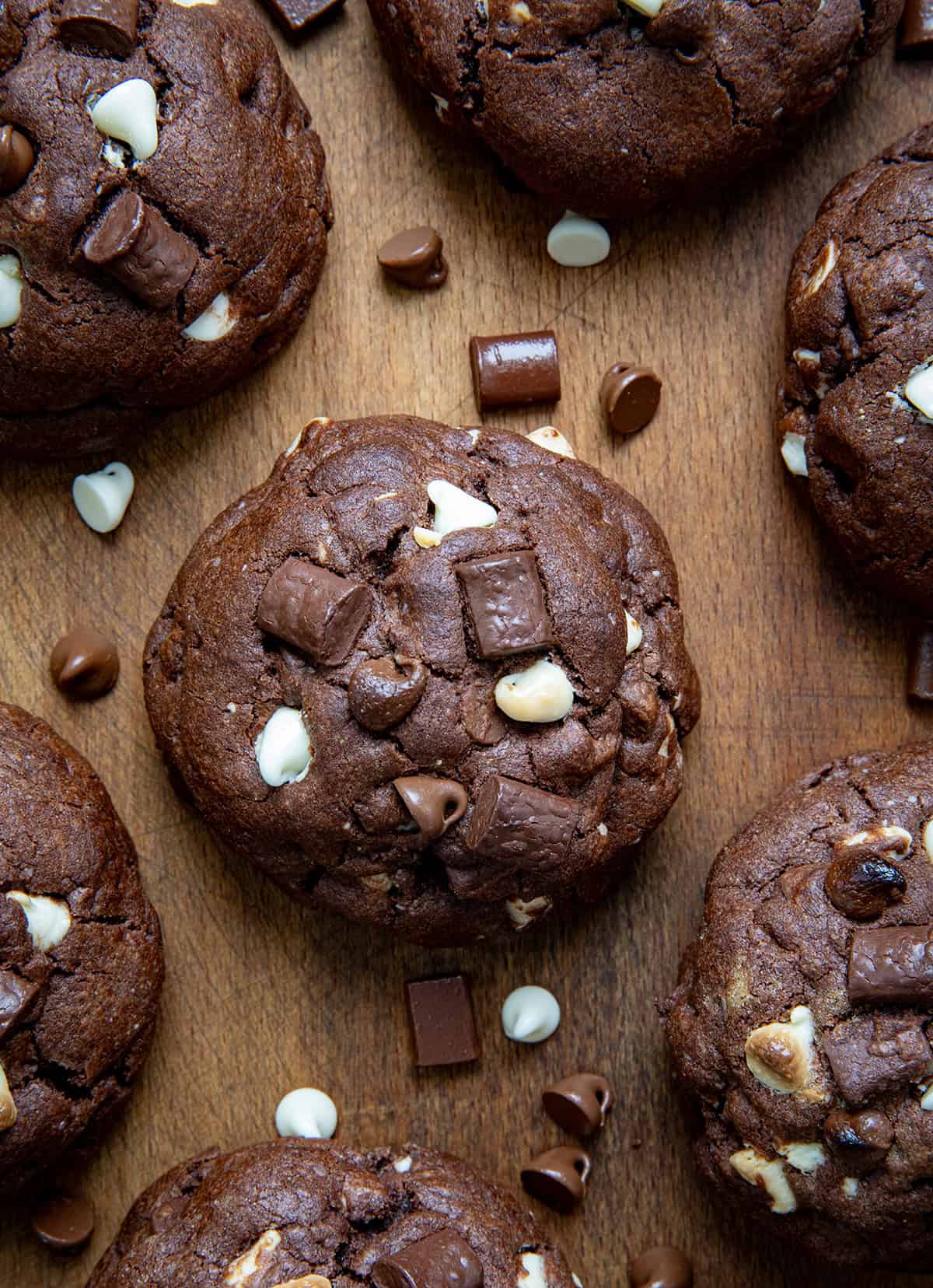 f you love my Ultimate Thick and Chewy Chocolate Chip Cookies, get ready for these Triple Chocolate Chunk Cookies! They are made with three kinds of chocolate (yes, three!), and that ultra-thick, soft-based texture you already know and love! Triple Chocolate Chunk Cookies laying flat on a wooden table with chocolate chunks and chips surrounding it.