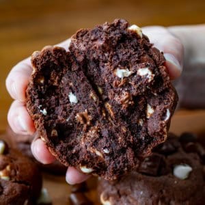 Hand holding a Triple Chocolate Chunk Cookie that has been broken in half showing just how thick and chewy it is.