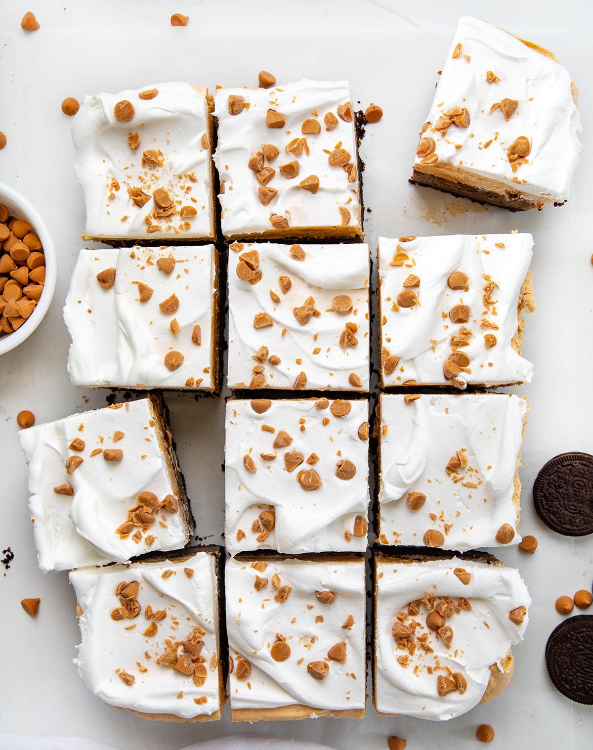 These Butterscotch Mud Bars have an Oreo cookie crust with a fudgy homemade brownie layer, topped with a silky smooth butterscotch mousse topping. I could eat each one of these layers as a dessert on its own, but putting them together creates a triple threat (in the best way!) of a dessert! Butterscotch Mud Bars cut into squares on a white table from overhead.