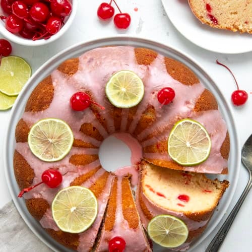Cherry Limeade Pound Cake on a white cake plate with some pieces cut and one on a plate from overhead.