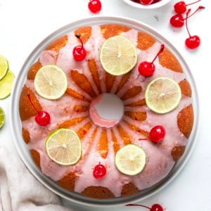Whole Cherry Limeade Pound Cake on a white cake plate on a white table from overhead.