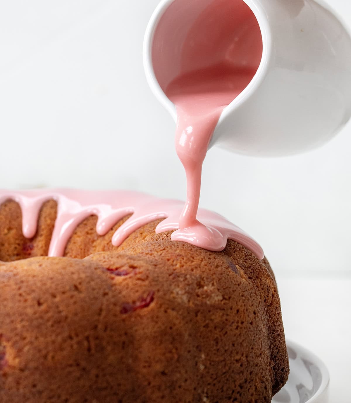 This Cherry Limeade Pound Cake is bursting with bright lime zest and sweet maraschino cherries, just like my favorite cherry limeade drink, but in cake form! I love how moist and tender it turns out! Pouring glaze over Cherry Limeade Cake.
