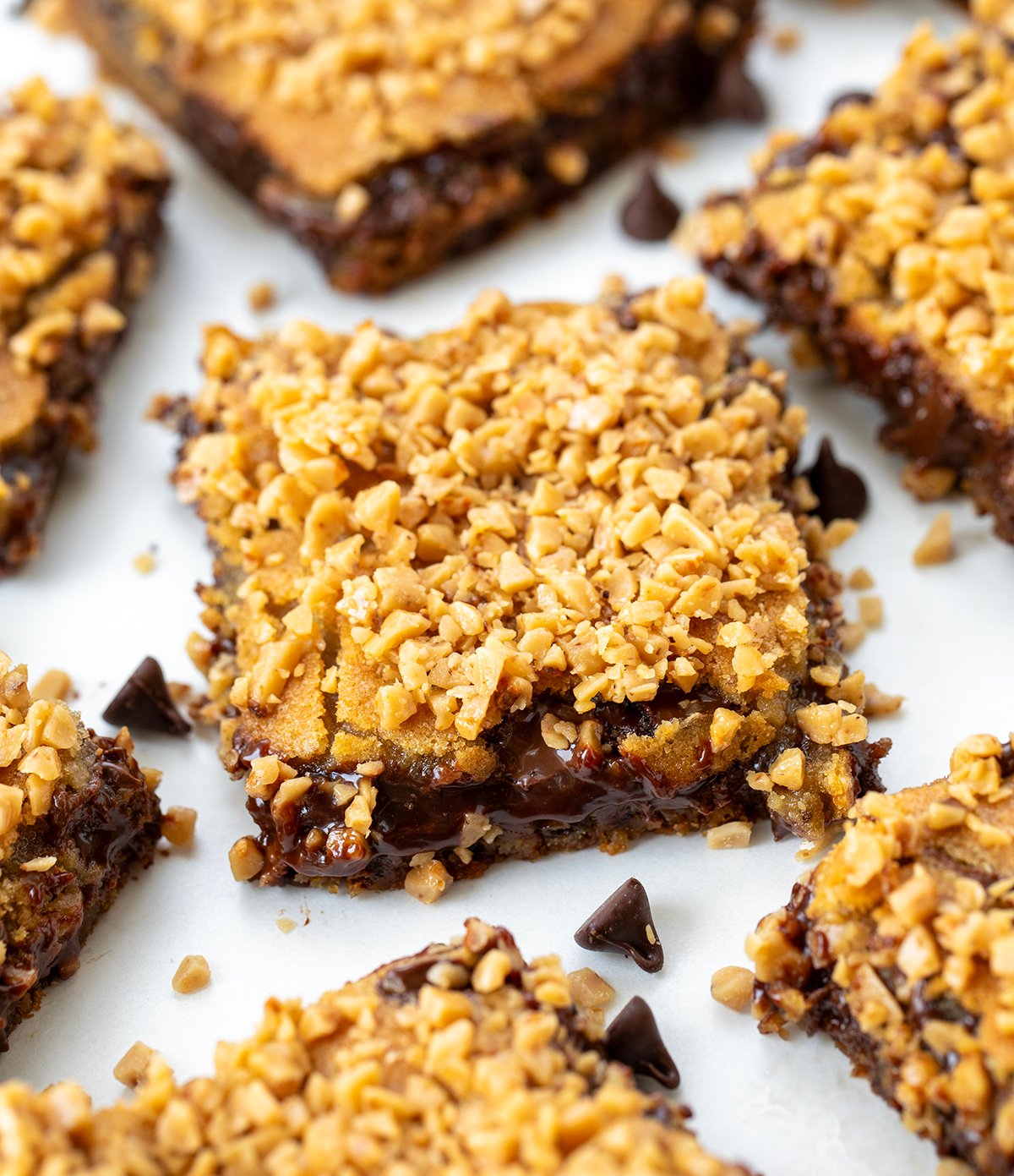 These Chocolate Chip Toffee Fudge Bars are rich, gooey, and packed with flavor! Made from my popular Hot Fudge Chocolate Chip Cookie Bars, this version adds sweet and crunchy English toffee bits for even more texture and buttery flavor! Chocolate Chip Toffee Fudge Bars on a white table spread out.