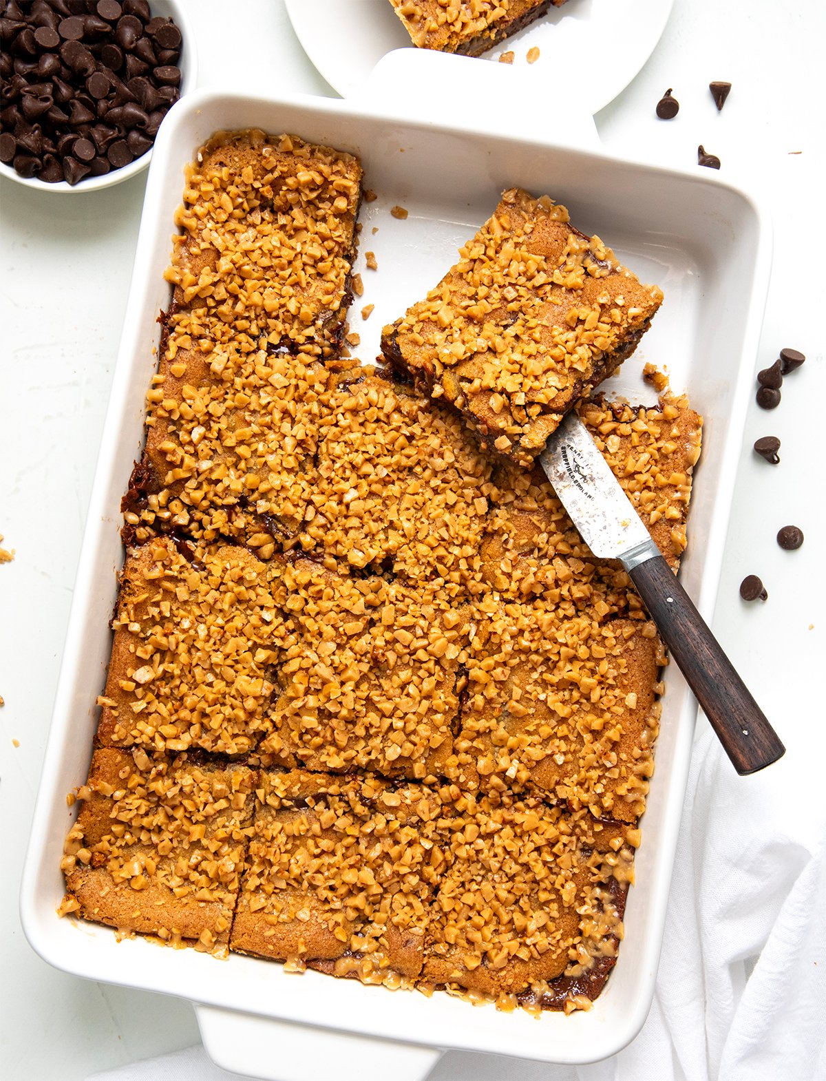 These Chocolate Chip Toffee Fudge Bars are rich, gooey, and packed with flavor! Made from my popular Hot Fudge Chocolate Chip Cookie Bars, this version adds sweet and crunchy English toffee bits for even more texture and buttery flavor! Pan of Chocolate Chip Toffee Fudge Bars cut up with a knife in the pan from overhead.