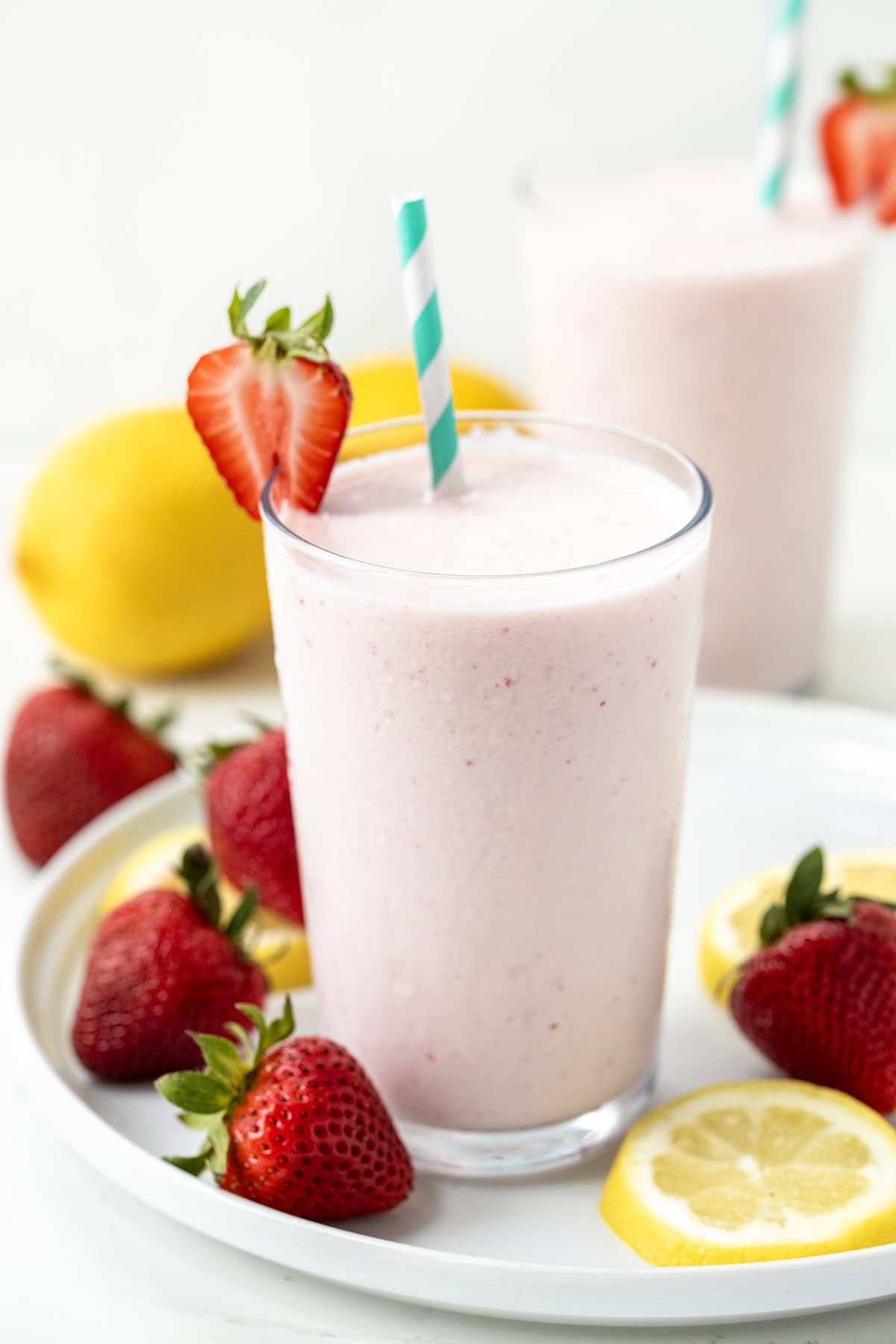 I'm all about beating the heat with this super simple, two-ingredient Frosted Strawberry Lemonade, the ultimate refreshing drink for hot summer days! This tangy 2-ingredient treat comes together in seconds and is perfect for kids and adults alike! Glasses of Frosted Strawberry Lemonade on a white platter with strawberries and lemons.