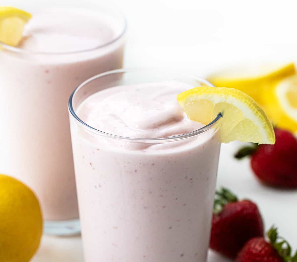 I'm all about beating the heat with this super simple, two-ingredient Frosted Strawberry Lemonade, the ultimate refreshing drink for hot summer days! This tangy 2-ingredient treat comes together in seconds and is perfect for kids and adults alike! Glasses of Frosted Strawberry Lemonade on a white platter with strawberries and lemons.