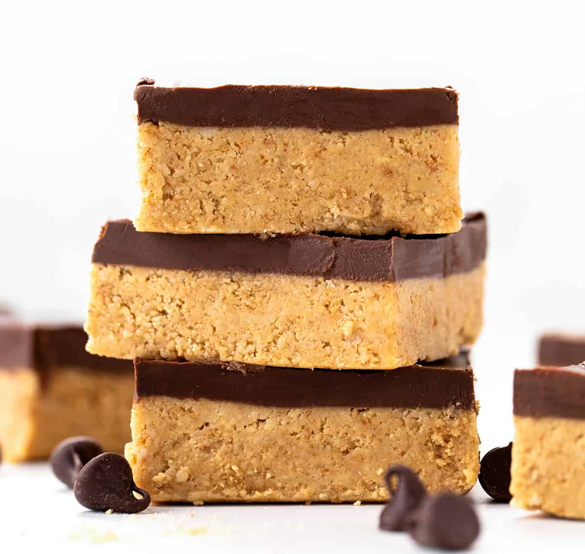Lunch Lady Peanut Butter Bars are a no-bake dessert with a crunchy graham cracker and peanut butter base topped with a smooth chocolate peanut butter topping. The bars set up in the refrigerator for an easy, delicious treat you can slice and enjoy anytime. Stack of Lunch Lady Peanut Butter Bars on a white table.