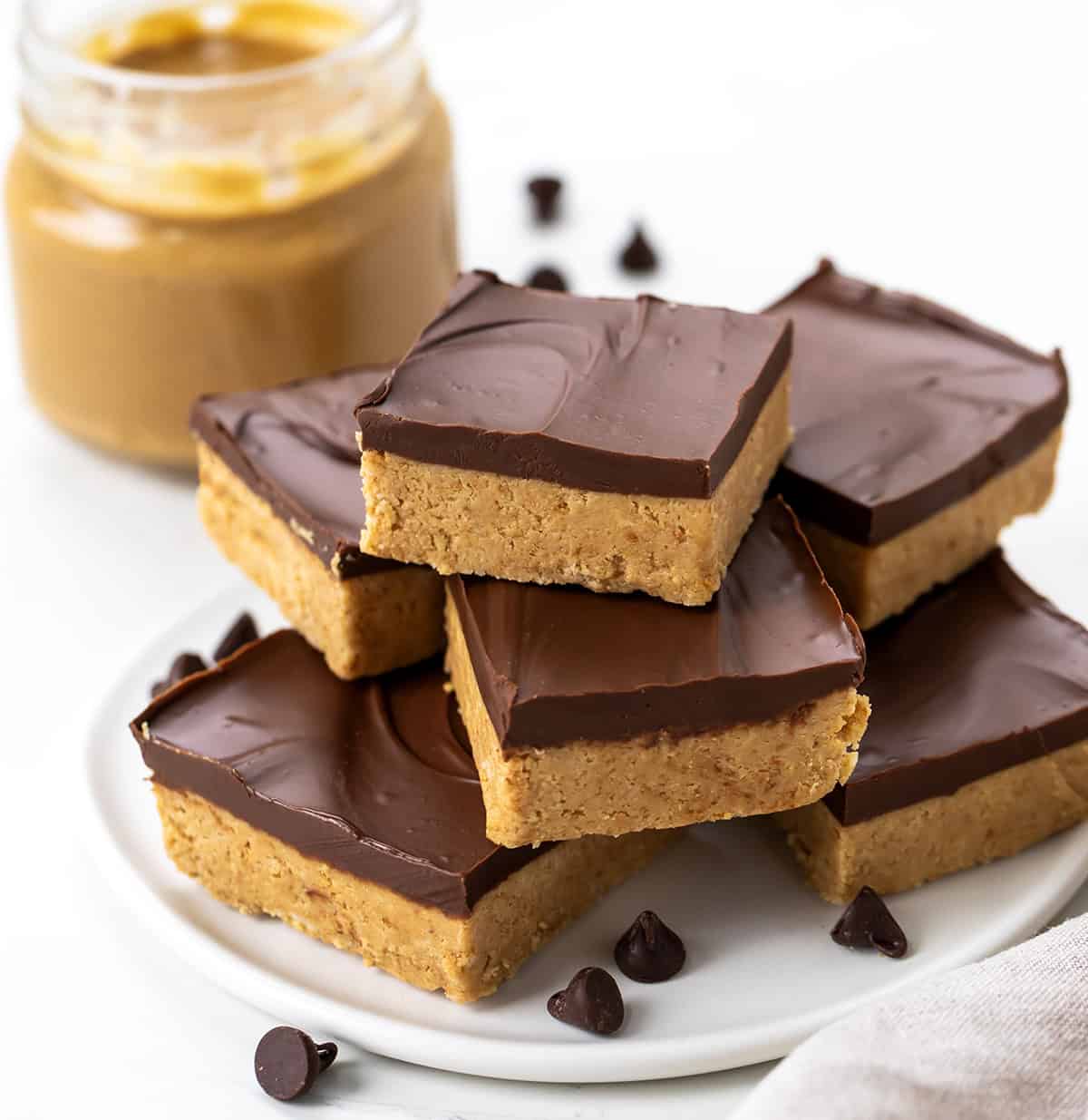 Lunch Lady Peanut Butter Bars are a no-bake dessert with a crunchy graham cracker and peanut butter base topped with a smooth chocolate peanut butter topping. The bars set up in the refrigerator for an easy, delicious treat you can slice and enjoy anytime. Platter stacked with Lunch Lady Peanut Butter Bars on a white table.