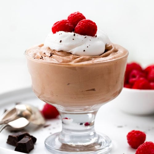 Glass of Nutella Mousse with whipped cream, fresh raspberries, and shaved chocolate on it.