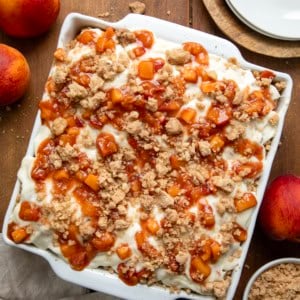 Pan of Peach Cobbler Cinnamon Rolls on a wooden table with fresh peaches from overhead.