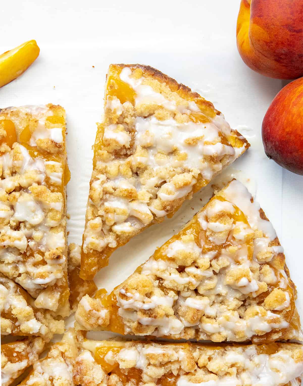 Anytime I see a dessert pizza like Cactus Bread, I want to skip the meal and go straight for the sweet stuff! This Peach Cobbler Pizza starts with my soft, fluffy focaccia bread. On top, you get sweet peaches, a buttery cinnamon crumble, and a drizzle of vanilla glaze. You wonโt want to share! Cut up Peach Cobbler Pizza with one slice askew on a white table from overhead.