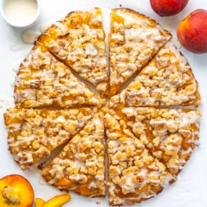 Peach Cobbler Pizza cut into slices on a white table.