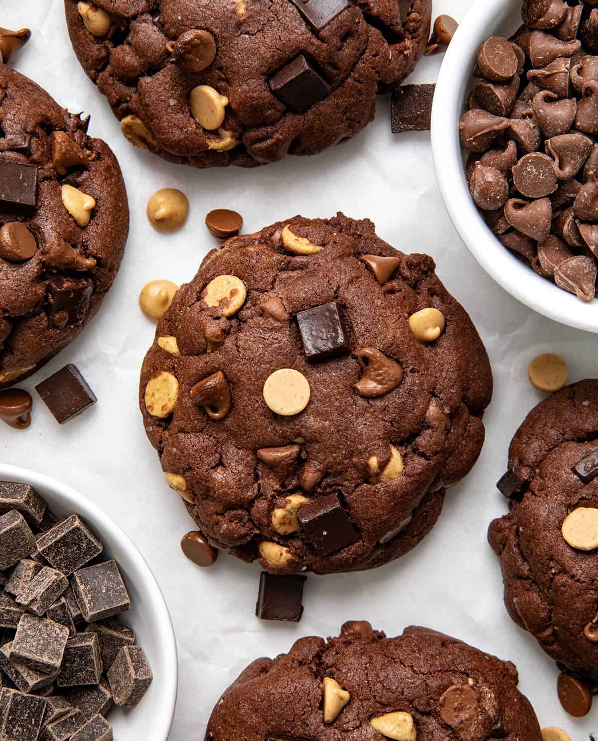 These Peanut Butter Chocolate Chunk Cookies are extra large, extra thick, bakery-style chocolate cookies loaded with semi-sweet chocolate, milk chocolate, and peanut butter chips! Peanut Butter Chocolate Chunk Cookies on a white table from overhead.