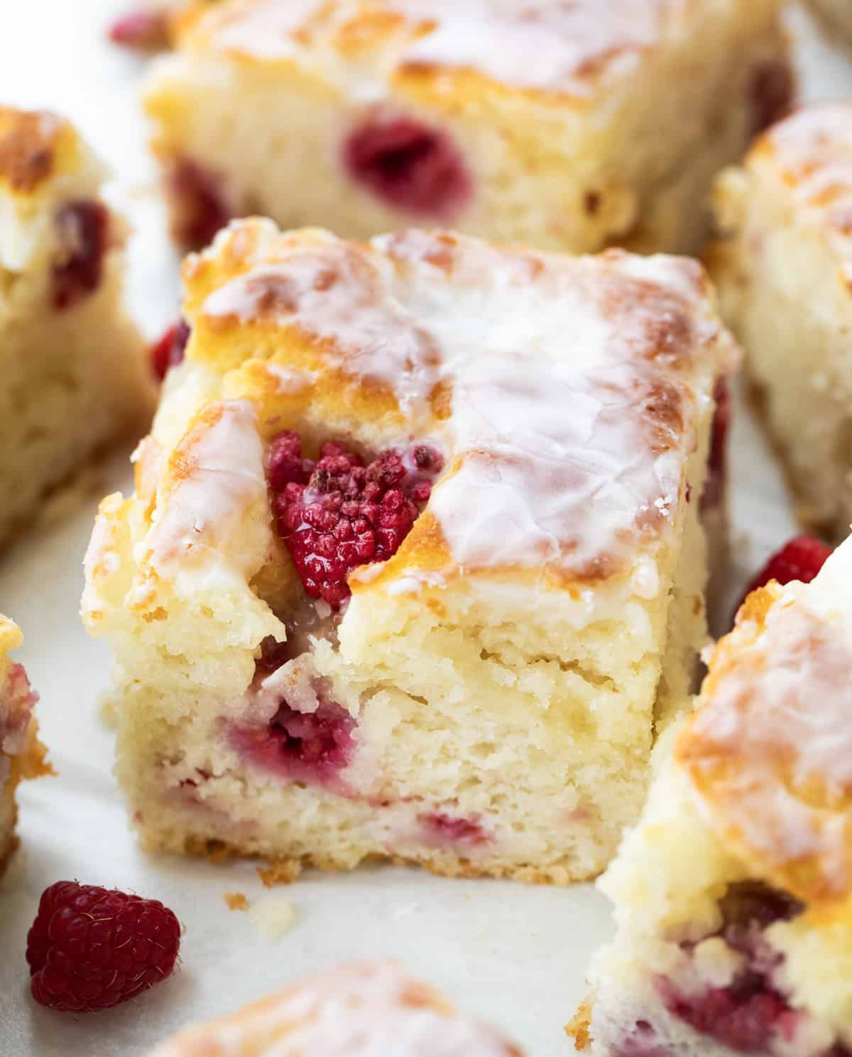 Soft, buttery Glazed Raspberry Butter Swim Biscuits are filled with juicy raspberries and baked right in melted butter for golden, crispy edges and a tender center. Topped with a sweet glaze, they are an easy, bakery-style treat made with simple ingredients with no rolling or cutting needed! Close up of a glazed Raspberry Butter Swim Biscuit.