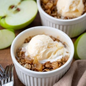 Single serve bowls of Apple Crisp on a wooden table with forks and fresh green apples.