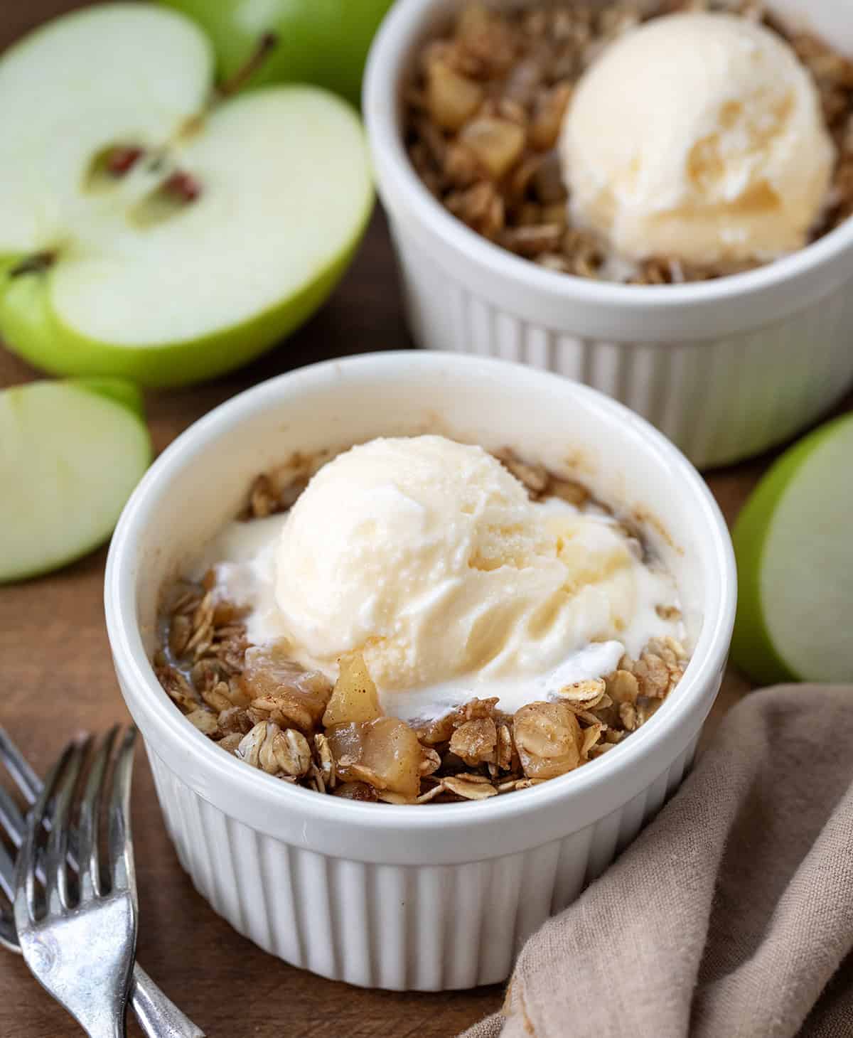 Craving a quick and satisfying dessert? This apple crisp is the perfect single-serve treat. Made with fresh apples and a simple brown sugar oat topping, it comes together in minutes, no oven needed! Single serve bowls of Apple Crisp on a wooden table with forks and fresh green apples.
