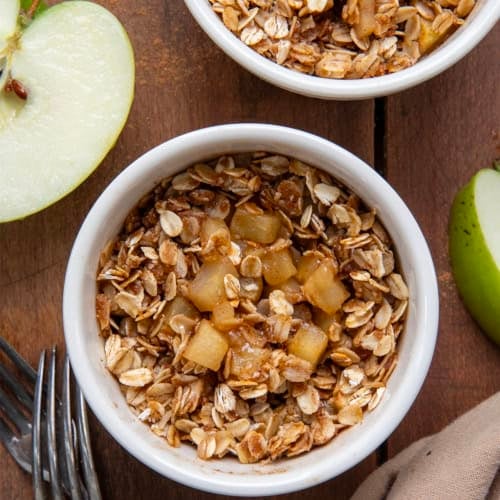 Close up of Single Serve Apple Crisp's on a wooden table with fresh cut apple.