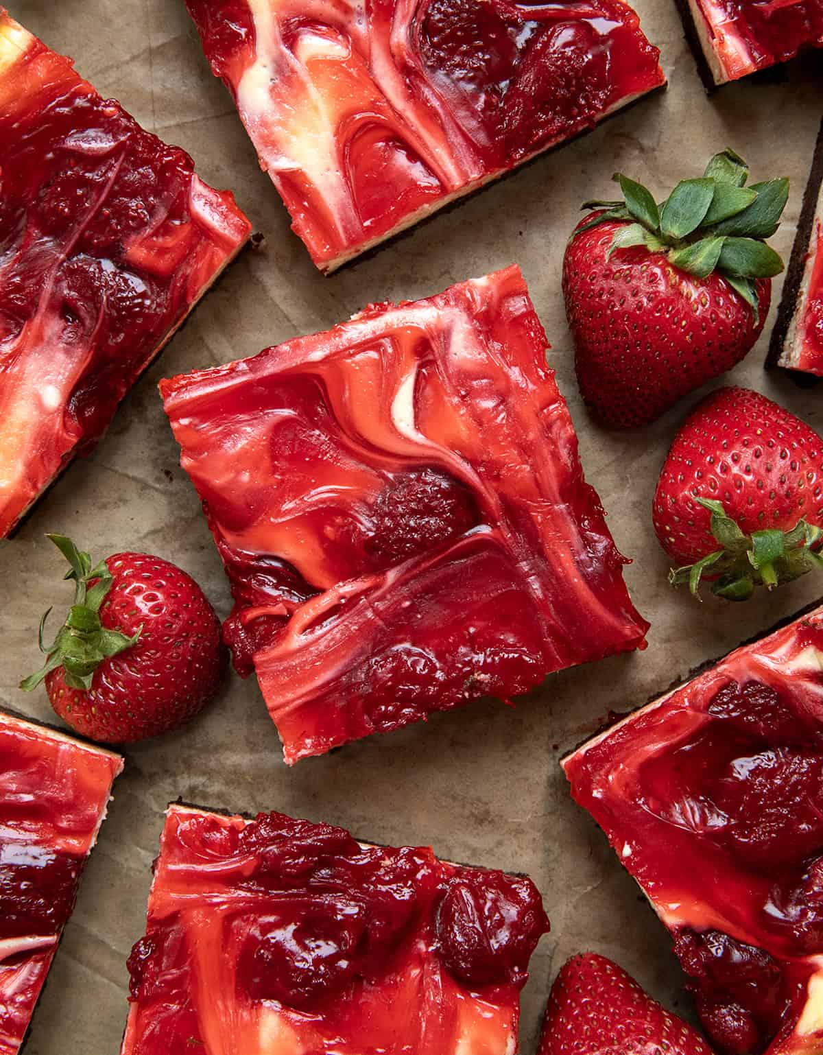 If youโre a fan of rich, fudgy brownies and creamy cheesecake, youโre going to fall hard for these Strawberry Cheesecake Brownies. Itโs like two desserts in one! Strawberry Cheesecake Brownies on a wooden table with fresh strawberries from overhead.