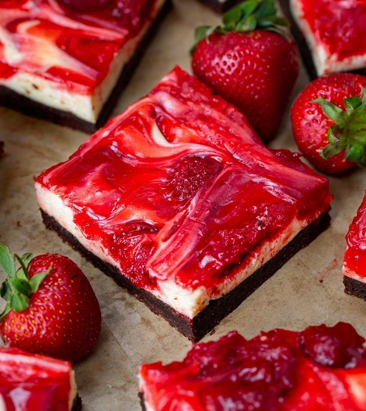 If youโre a fan of rich, fudgy brownies and creamy cheesecake, youโre going to fall hard for these Strawberry Cheesecake Brownies. Itโs like two desserts in one! Close up of a Strawberry Cheesecake Brownie next to other brownies and fresh strawberries.