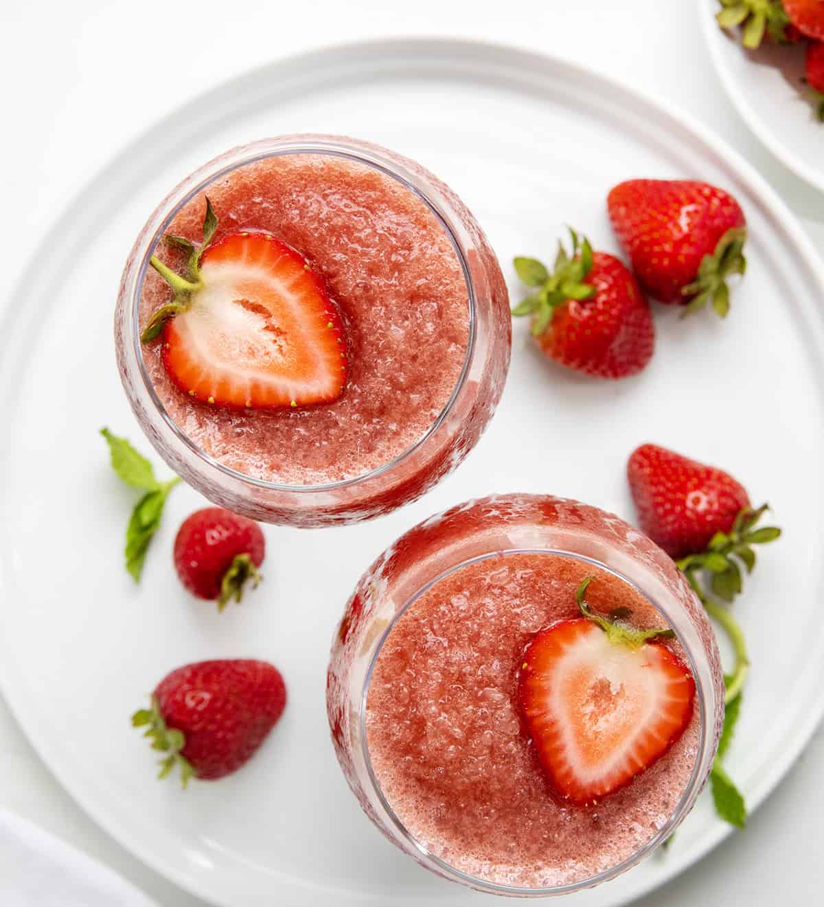 This Strawberry Frosé is cold, fruity, and just what you need (yes, need 😜) on a warm day. Made with frozen strawberries, chilled rosé, and a little sugar, it blends into a smooth, slushy drink that’s perfect for sipping on the patio or sharing with friends! Glasses of Strawberry Frose on a white platter from overhead.