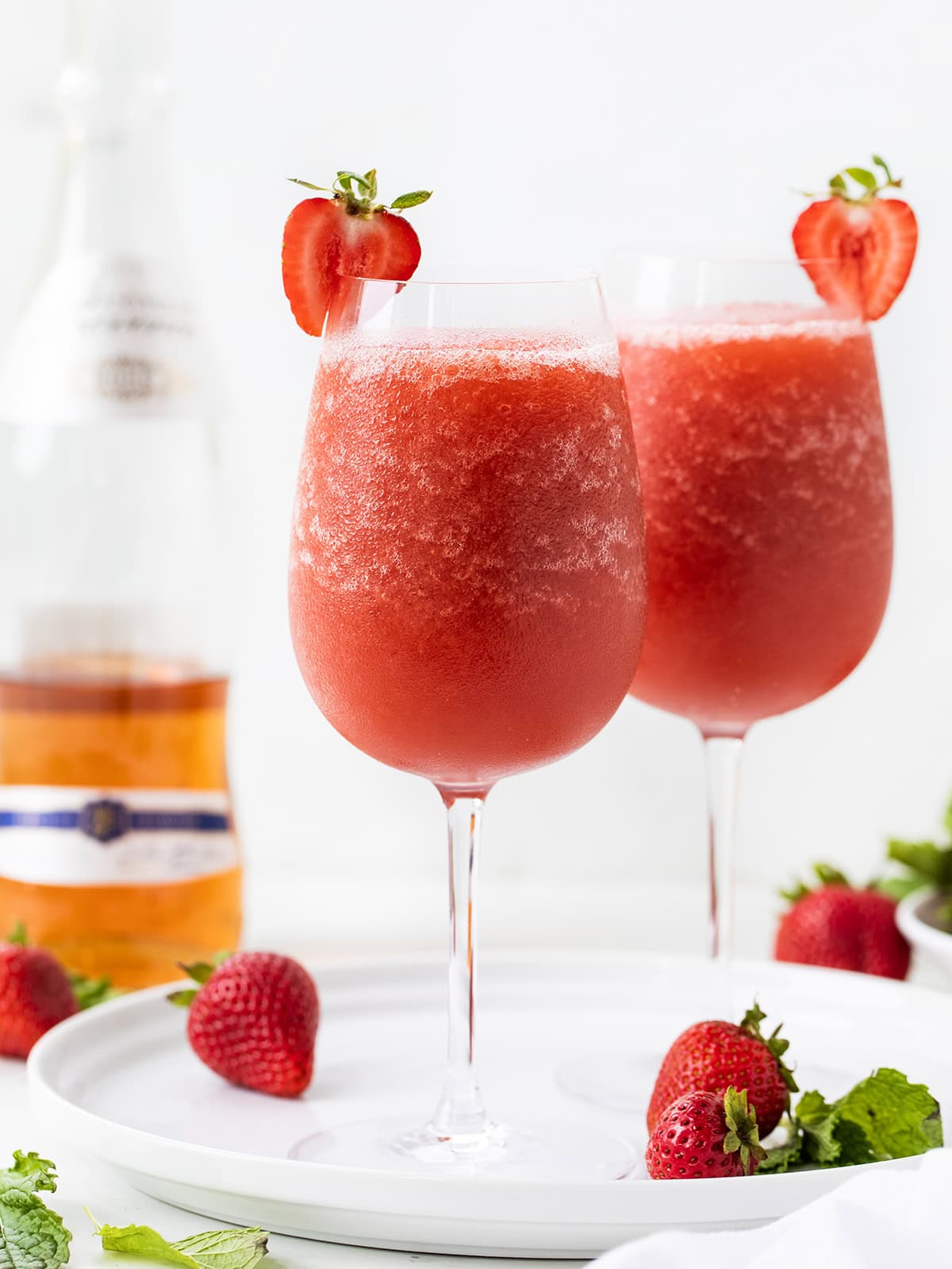 This Strawberry Frosé is cold, fruity, and just what you need (yes, need 😜) on a warm day. Made with frozen strawberries, chilled rosé, and a little sugar, it blends into a smooth, slushy drink that’s perfect for sipping on the patio or sharing with friends! Glasses of Strawberry Frose on a white platter on a white table.