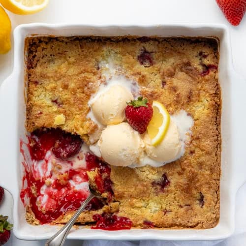 White pan of Strawberry Lemon Dump Cake with a portion removed and ice cream melting.