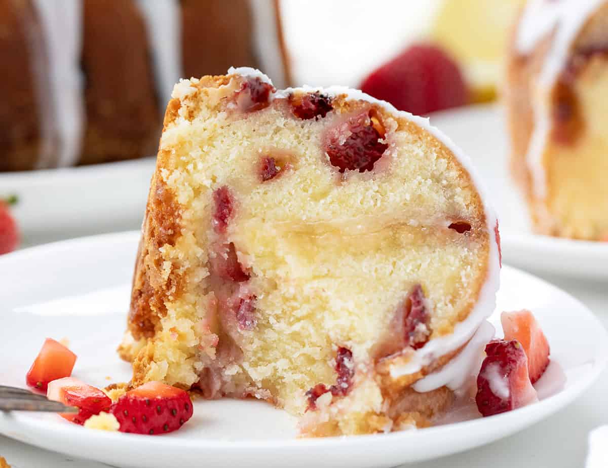 Strawberry Lemon Pound Cake is a moist and buttery homemade pound cake filled with fresh strawberries, bright lemon flavor, and topped with a tangy lemon glaze. Itโs the perfect spring or summer dessert! Slice of Strawberry Lemon Pound Cake on a white plate with a bite taken out and a fork resting on the plate.