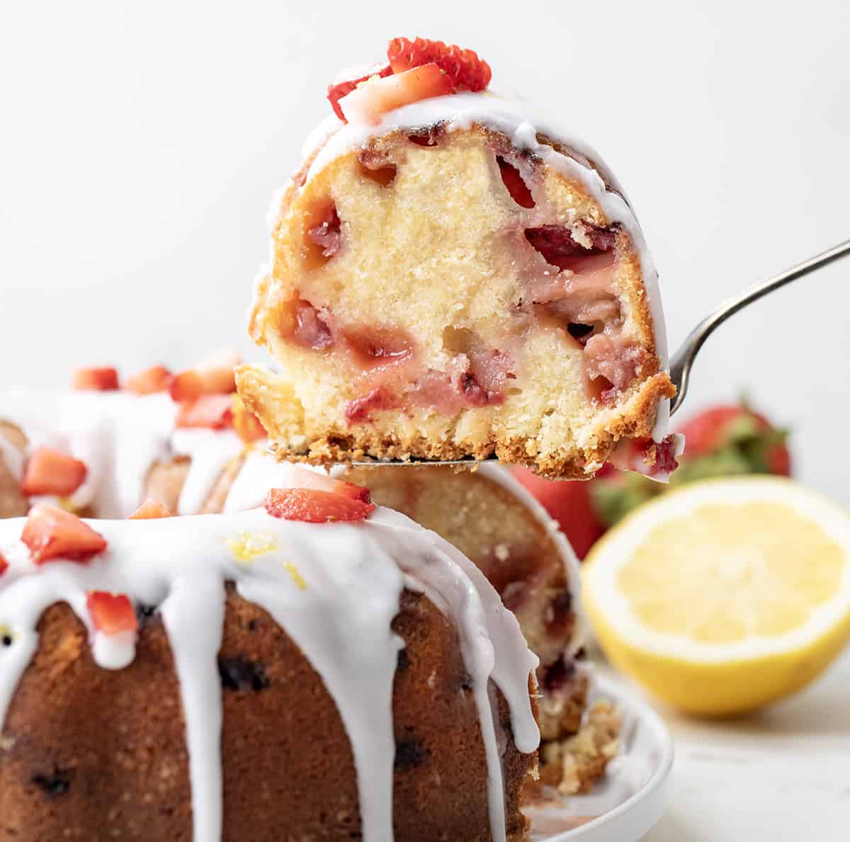 Strawberry Lemon Pound Cake is a moist and buttery homemade pound cake filled with fresh strawberries, bright lemon flavor, and topped with a tangy lemon glaze. Itโs the perfect spring or summer dessert! Picking up a piece of Strawberry Lemon Pound Cake from the cake plate.
