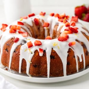 Whole Strawberry Lemon Pound Cake on a white cake plate on a white table close up.