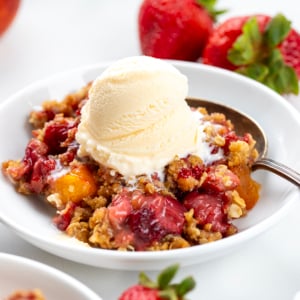 Bowl of Strawberry Peach Crisp on a white table with a spoon in the bowl.