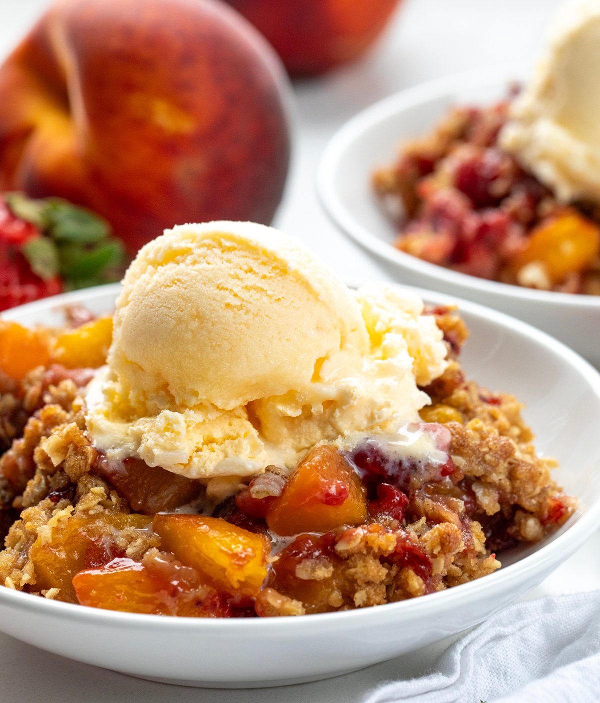 This Strawberry Peach Crisp is the perfect summer dessert, made with juicy, sweet strawberries and ripe peaches baked under a buttery oat topping with warm cinnamon and brown sugar. Every bite is bursting with fruit flavor and a crumbly texture. I love how easy this recipe is to throw together! Close up of Strawberry Peach Crisp with a scoop of ice cream on it.