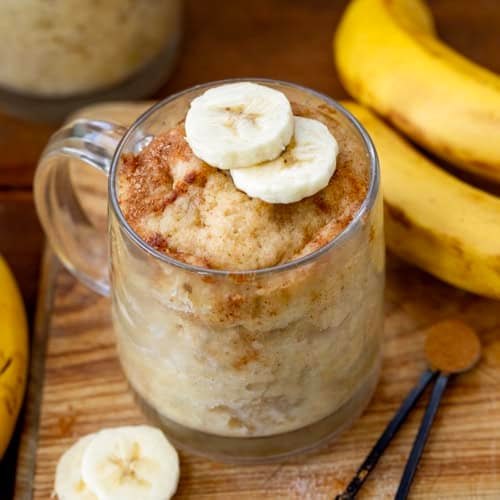 Banana Mug Cakes on a wooden table with fresh cut bananas.