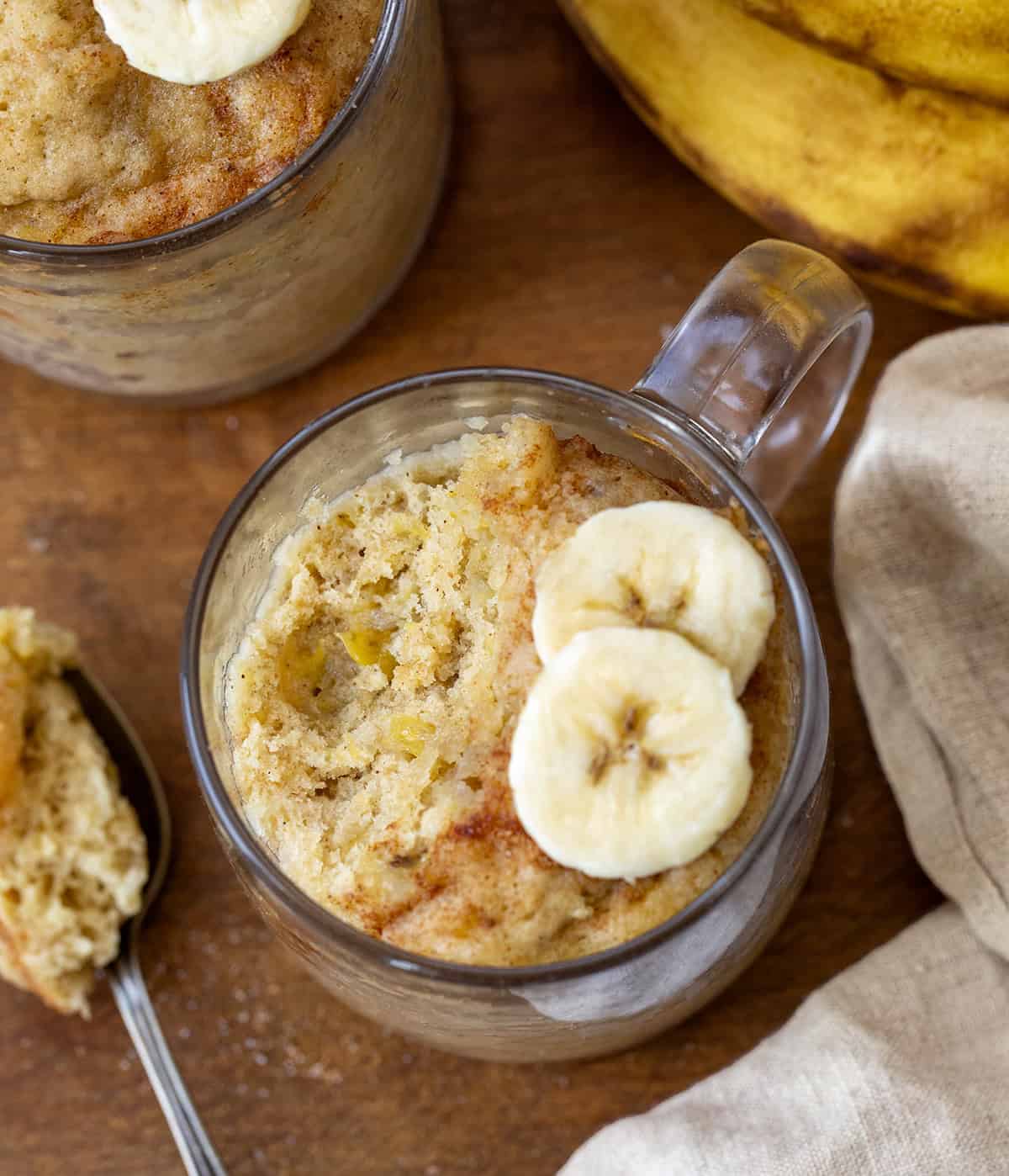 This microwave Banana Mug Cake is a quick and easy way to enjoy all the classic flavors of banana bread, packed with plenty of banana goodness and a warm touch of cinnamon. Ready in just minutes, it’s the perfect cozy dessert without any fuss! Banana Mug Cake on a wooden table with a bite removed showing texture of cake inside mug.