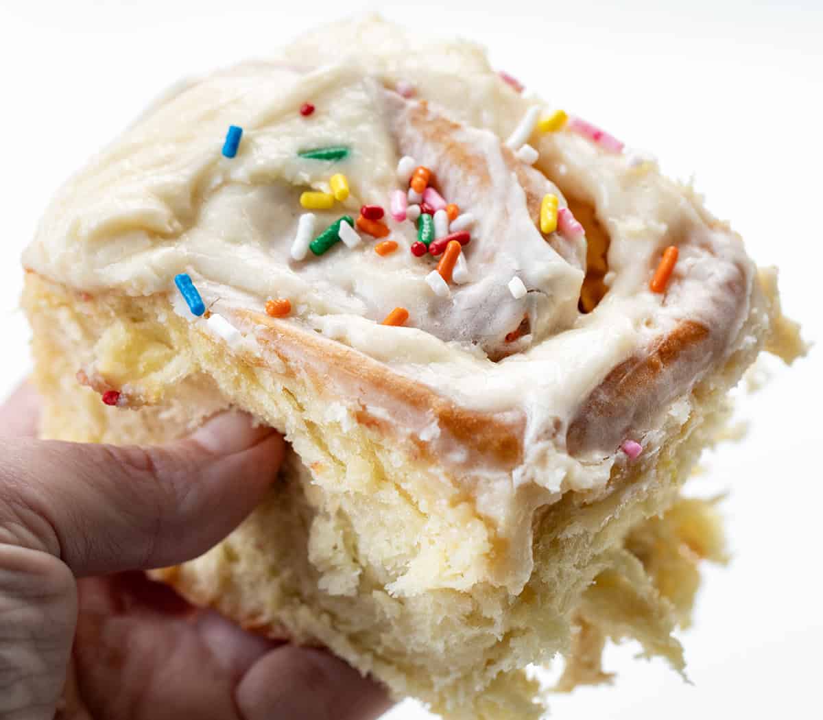 Celebrate every day like it's your birthday with these Birthday Cake Cinnamon Rolls! Soft, fluffy, mile-high rolls, like my classic cinnamon rolls, are filled with a sweet, buttery brown sugar mixture and loaded with colorful rainbow sprinkles that bring fun and festive flavor to every bite! Hand holding a Birthday Cake Cinnamon Roll.