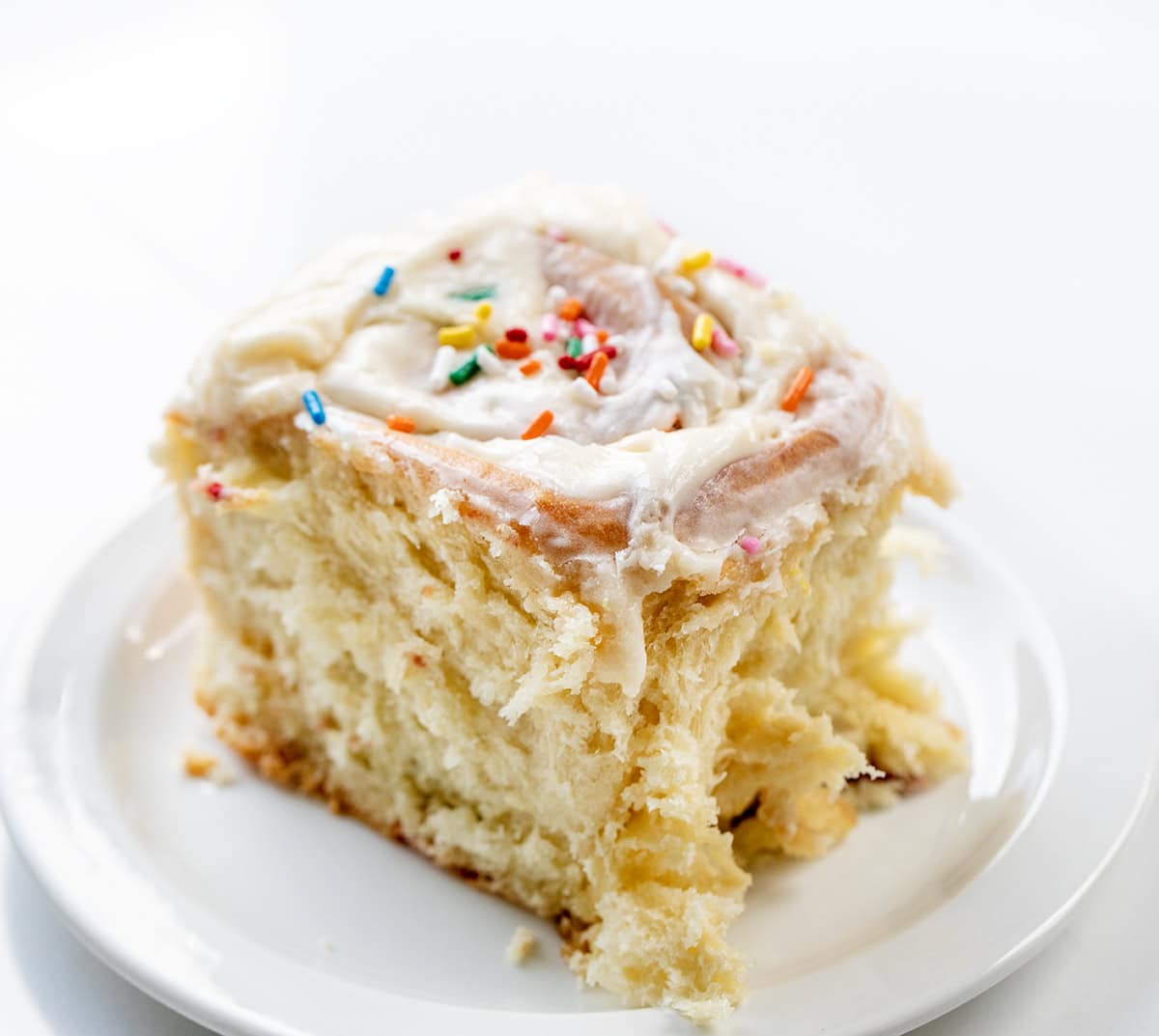 Celebrate every day like it's your birthday with these Birthday Cake Cinnamon Rolls! Soft, fluffy, mile-high rolls, like my classic cinnamon rolls, are filled with a sweet, buttery brown sugar mixture and loaded with colorful rainbow sprinkles that bring fun and festive flavor to every bite! Birthday Cake Cinnamon Roll on a white plate.