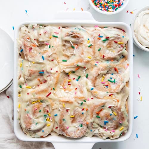Pan of Birthday Cake Cinnamon Rolls on a white table from overhead.