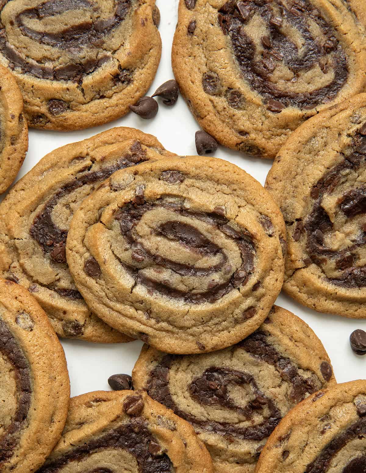 These semi-homemade Brownie Cookie Swirls combine classic chocolate chip dough with rich, fudgy brownie batter in one delicious treat! They are soft, chewy, full of chocolatey goodness, and surprisingly easy to make with just a handful of ingredients! Close up of Brownie Cookie Swirls laying on a white table with chocolate morsels.