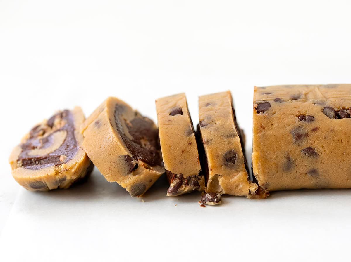 These semi-homemade Brownie Cookie Swirls combine classic chocolate chip dough with rich, fudgy brownie batter in one delicious treat! They are soft, chewy, full of chocolatey goodness, and surprisingly easy to make with just a handful of ingredients! Raw cookie dough batter filled with brownie batter that is being sliced to make individual cookies.