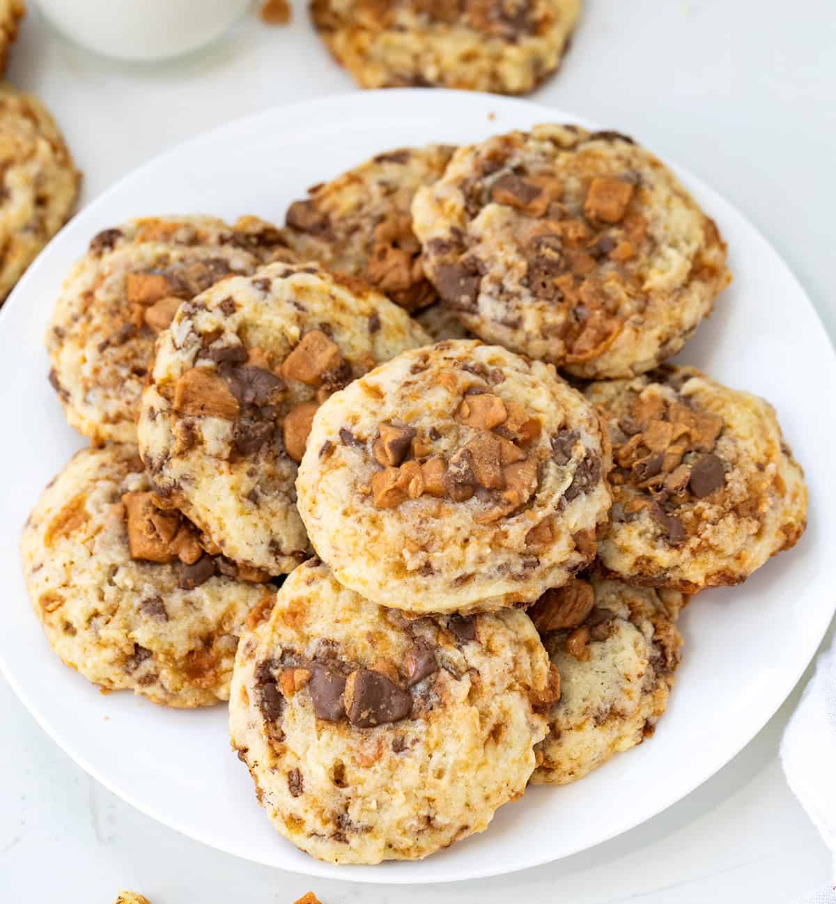 White plate of Butterfinger Cookies on a white table with milk.