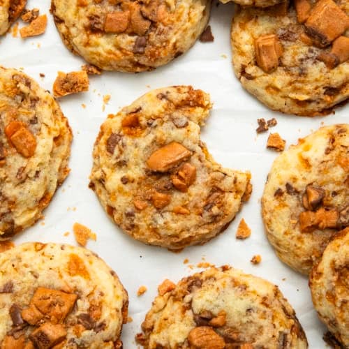 Butterfinger Cookies on a white table with the center cookie having a bite taken out of it.
