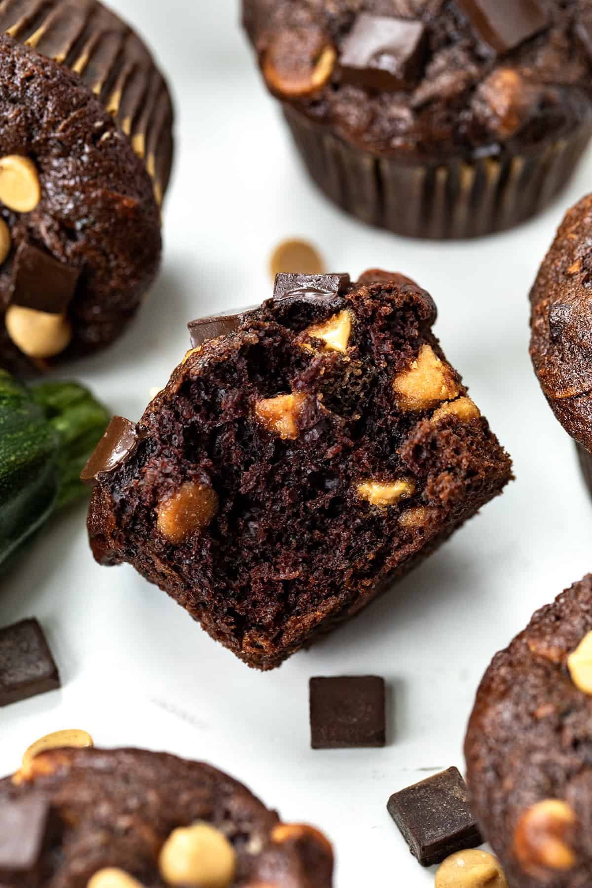 Halved Chocolate Peanut Butter Zucchini Muffin on a white table with other muffins nearby.