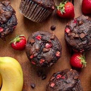Chocolate Strawberry Banana Muffins on a wooden table with fresh strawberries and a banana from overhead.