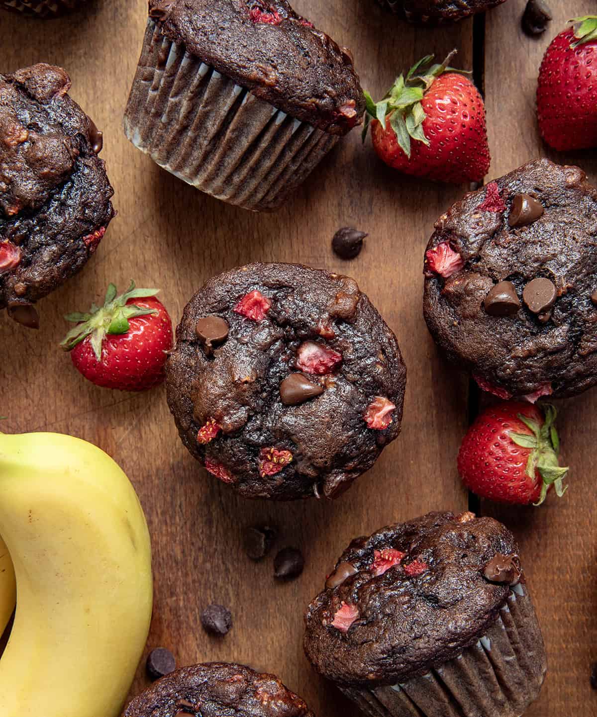 Chocolate Strawberry Banana Muffins on a wooden table with fresh strawberries and a banana from overhead.