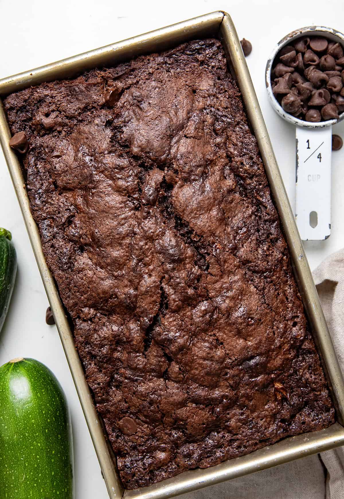 This Chocolate Zucchini Bread is rich, moist, and loaded with melty chocolate chips! Proof that veggies and dessert really can be best friends. With deep cocoa flavor, a perfectly tender crumb, and just the right amount of sweetness, you’d never guess there’s zucchini hiding inside! Loaf of Chocolate Zucchini Bread in the pan on a wooden table from overhead.