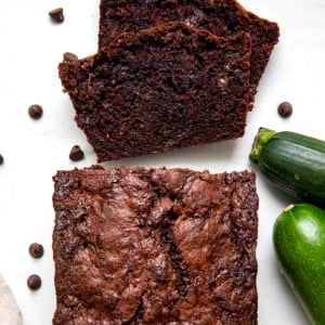 Loaf of Chocolate Zucchini Bread on a white table with a couple of pieces cut and laying flat.